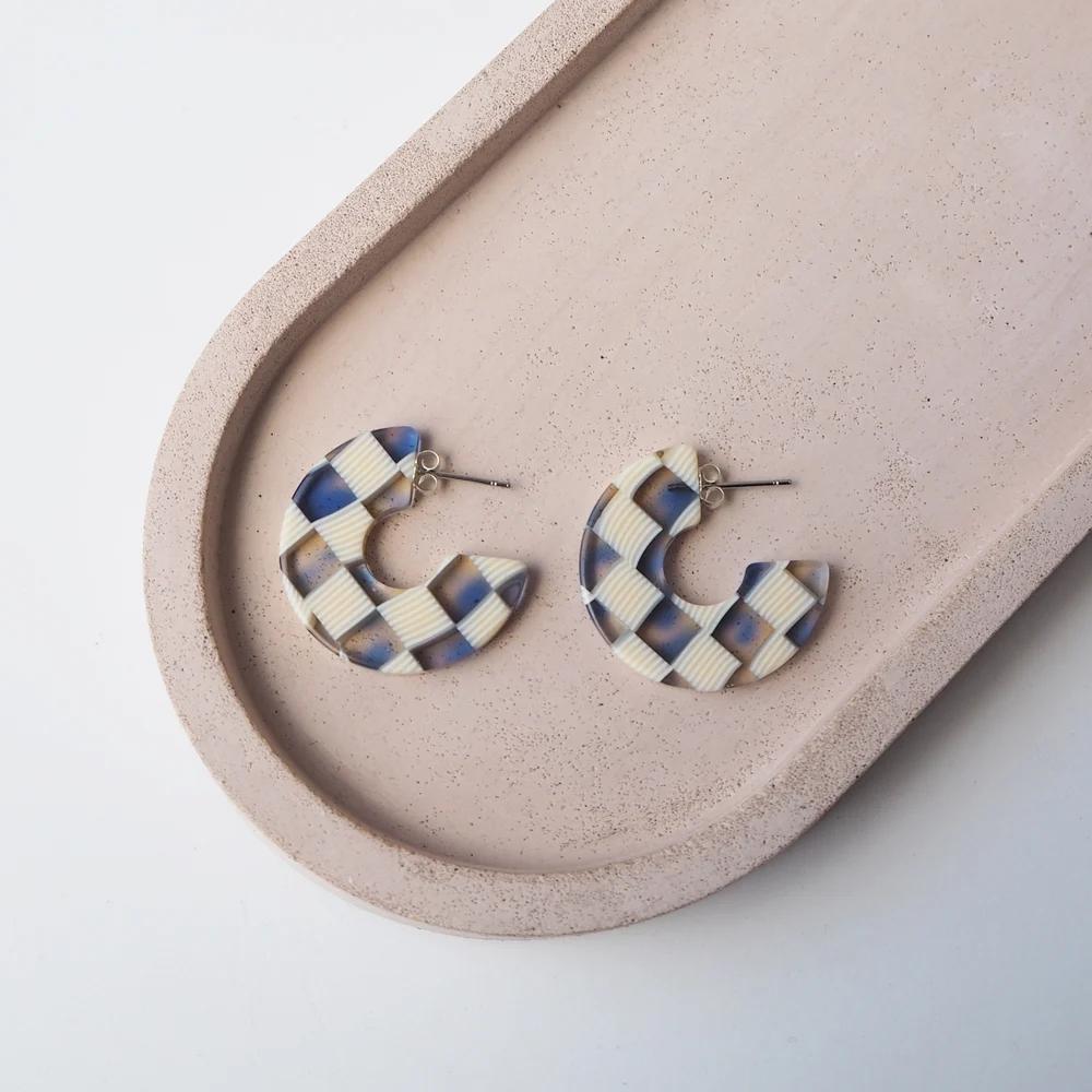 A pair of small acrylic hoop earrings in a mix of clear, blue and dark brown lying flat on a ceramic dish