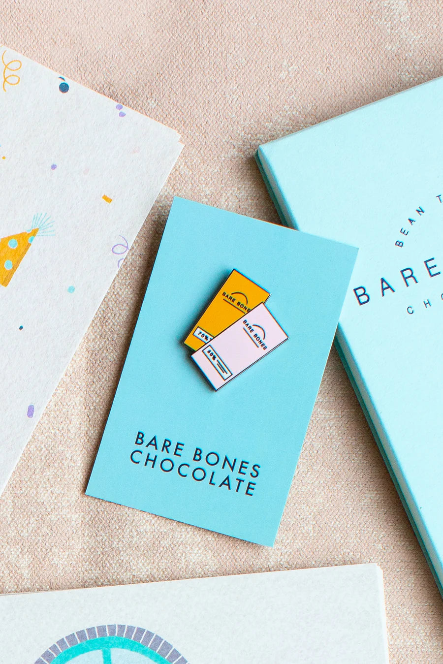 Bare Bones Chocolate pin badge with a chocolate bar design on a beige surface