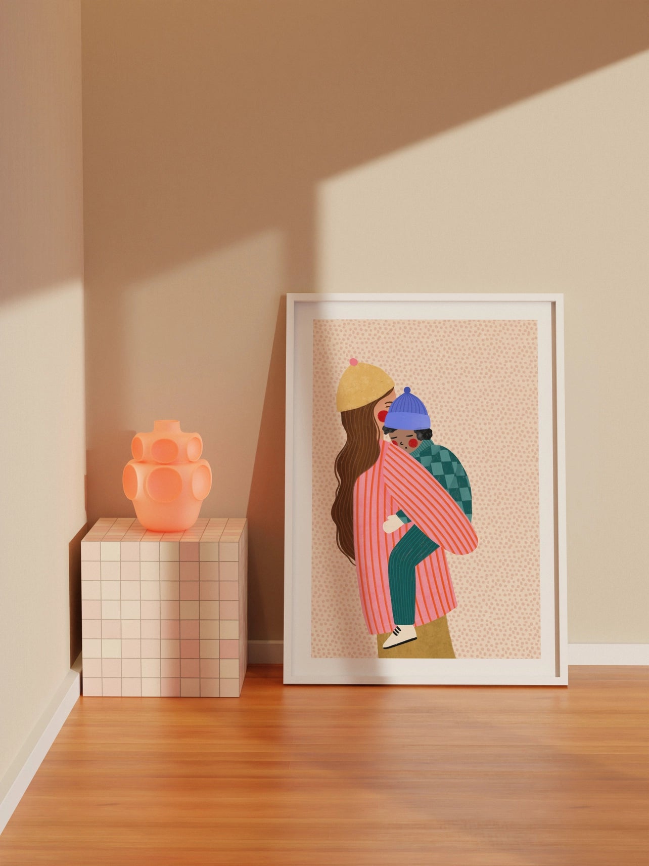 Framed artwork of two people hugging on a beige wall with a pink vase on a wooden block.
