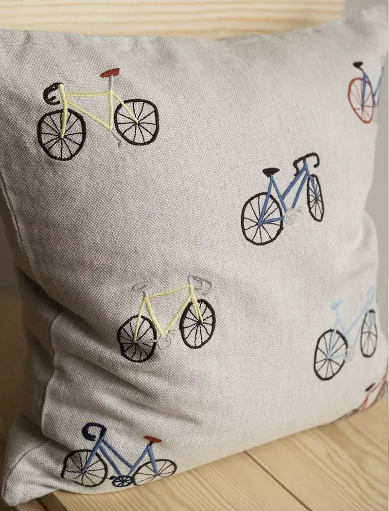 A square linen cushion with wobbly bicycle illustrations embroidered on the front by Fine Little Day