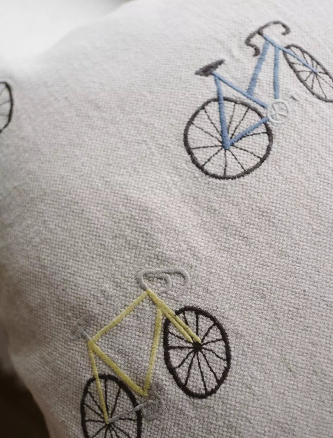 A square linen cushion with wobbly bicycle illustrations embroidered on the front by Fine Little Day