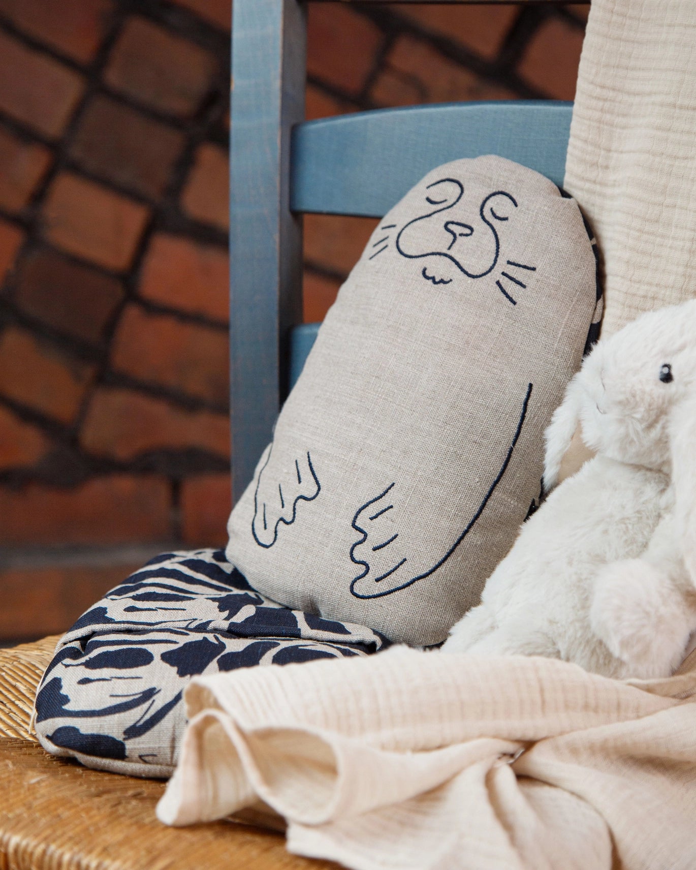 Blästa Henriët Linen Wheat & Lavender Bag Friend in embroidered Sal the seal design leaning upright on a blue chair next to a toy rabbit