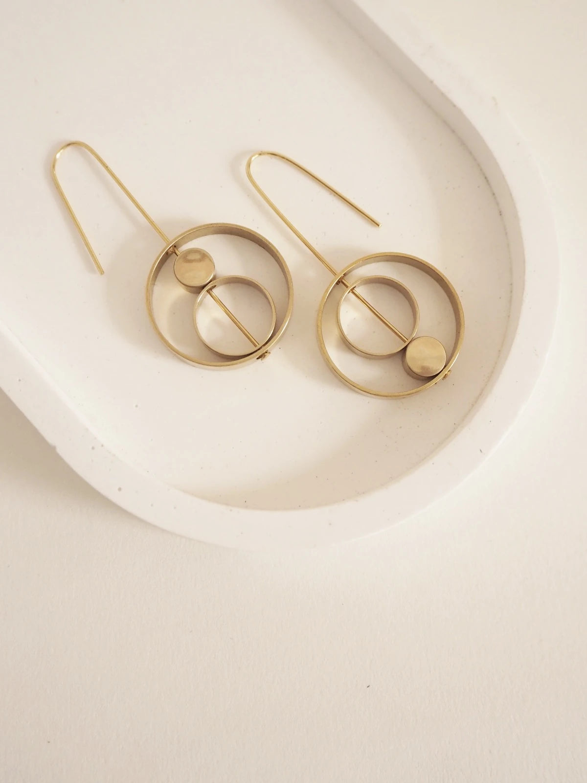 Nucleo Brass Rings within Rings Earrings by brass+bold, displayed on a white ceramic tray against a light beige background.