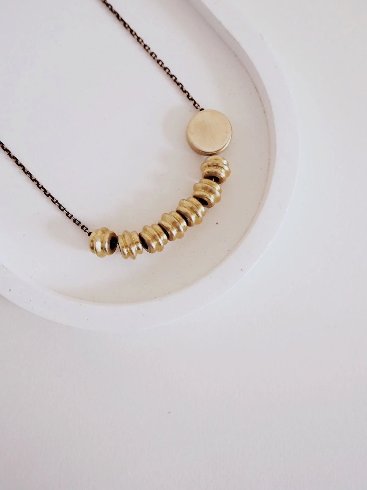 A close-up of Nucleo Solid Brass Totems and Brass Disc Necklace by brass+bold, resting on a white surface.