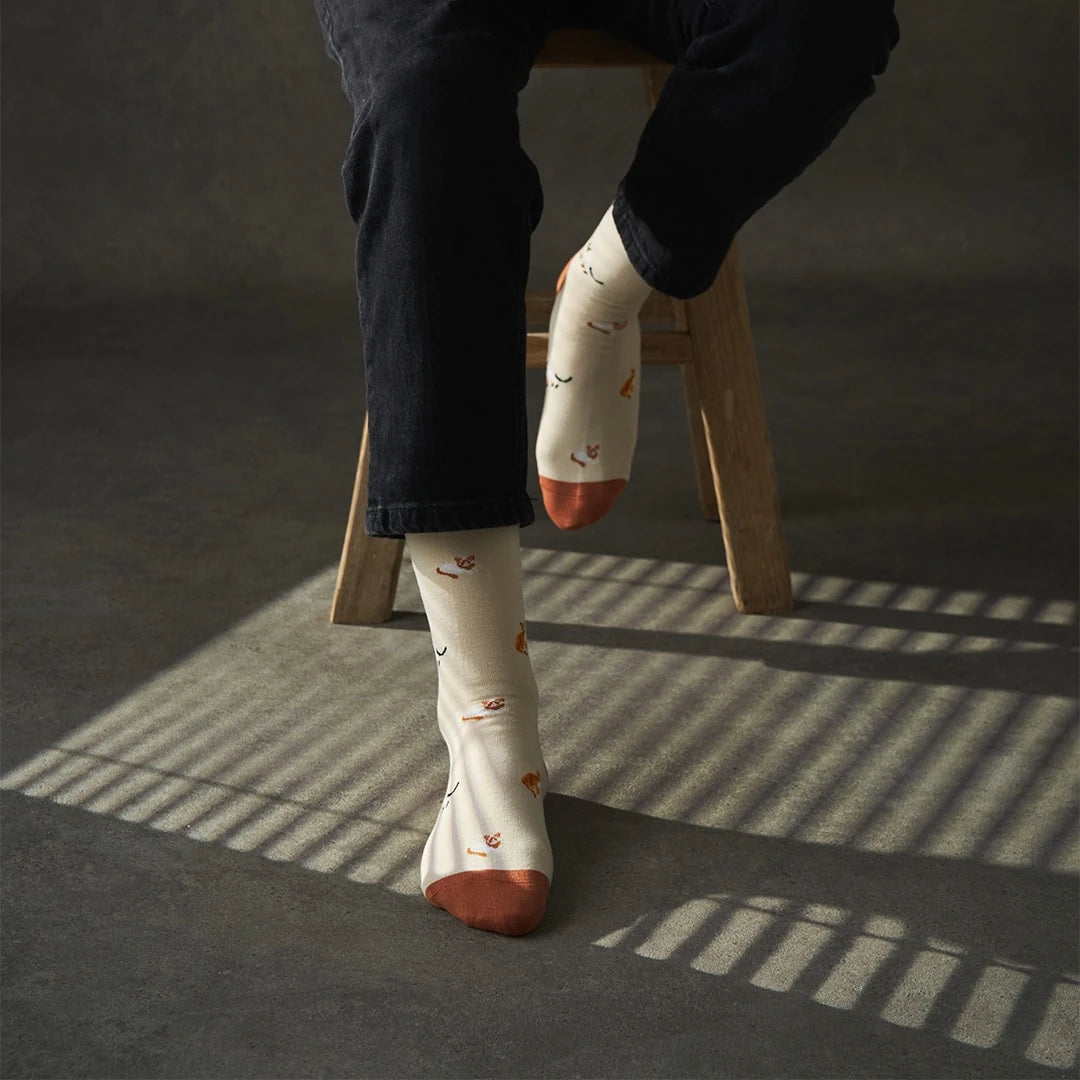 Person wearing KOSI London Bamboo Cat socks, sitting on a wooden stool.