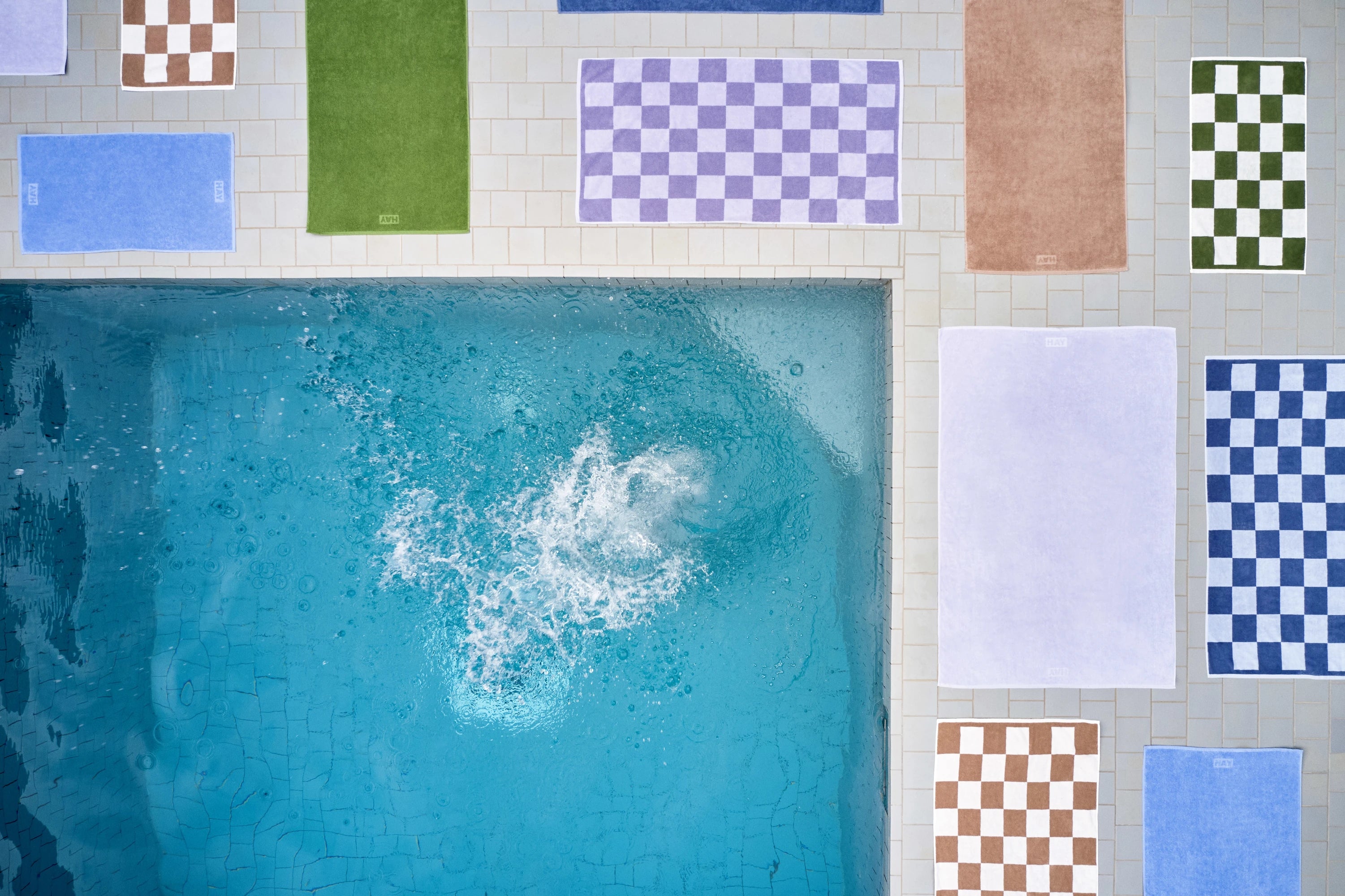 HAY Organic Cotton Check Towel and Mono Towel collection lying flat surrounding a pool