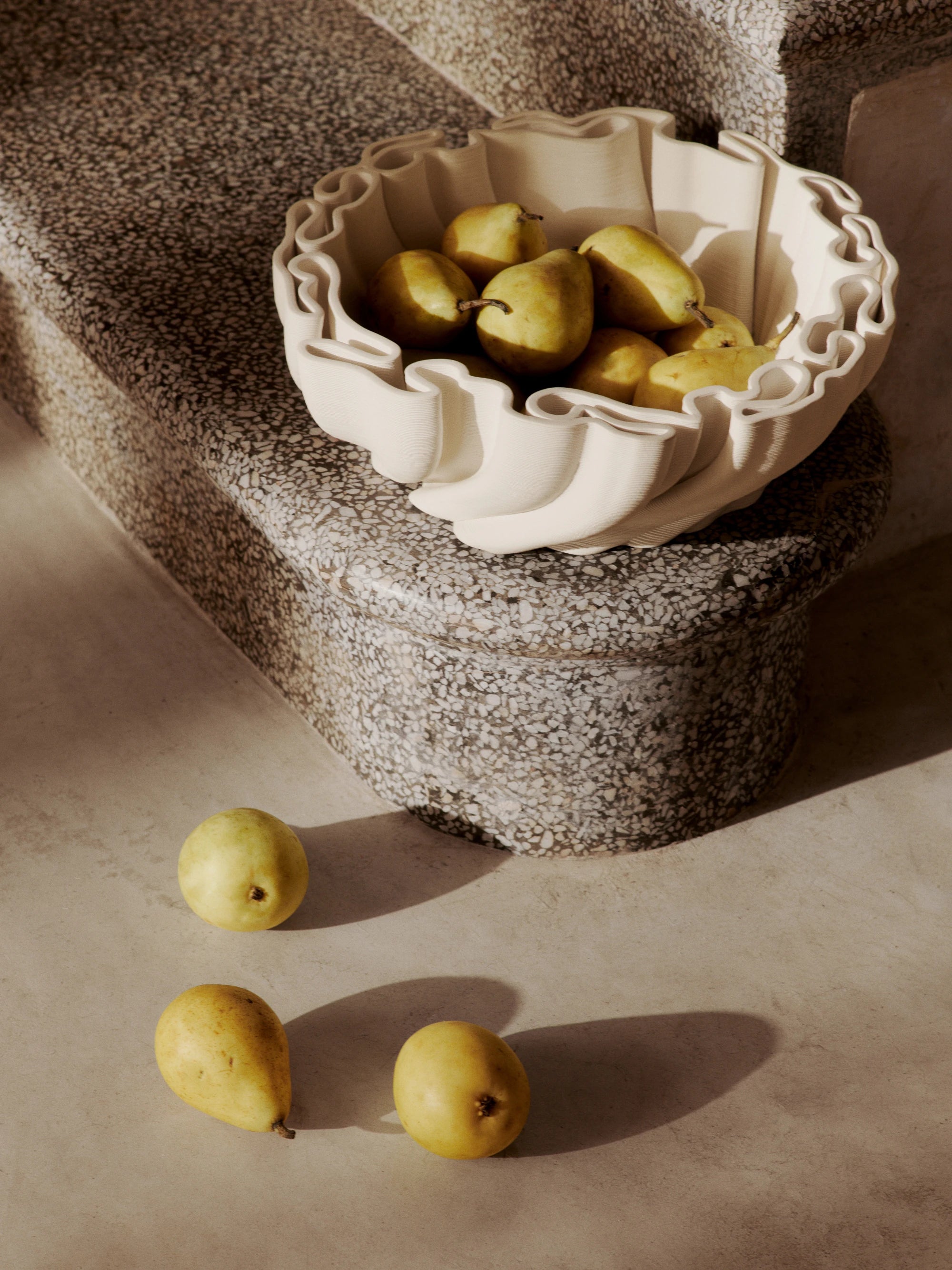 Ferm Living Dedali Bowl in Off-White 3D Printed Stoneware filled with and next to pears, sitting on a marble step