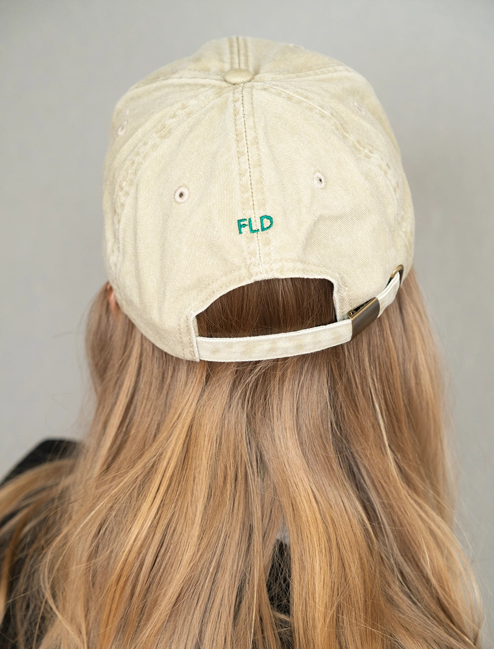 Back view of the Fine Little Day Embroidered 'Leaves' 6 Panel Cap in Vintage Beige being worn by a model with long hair against a grey background