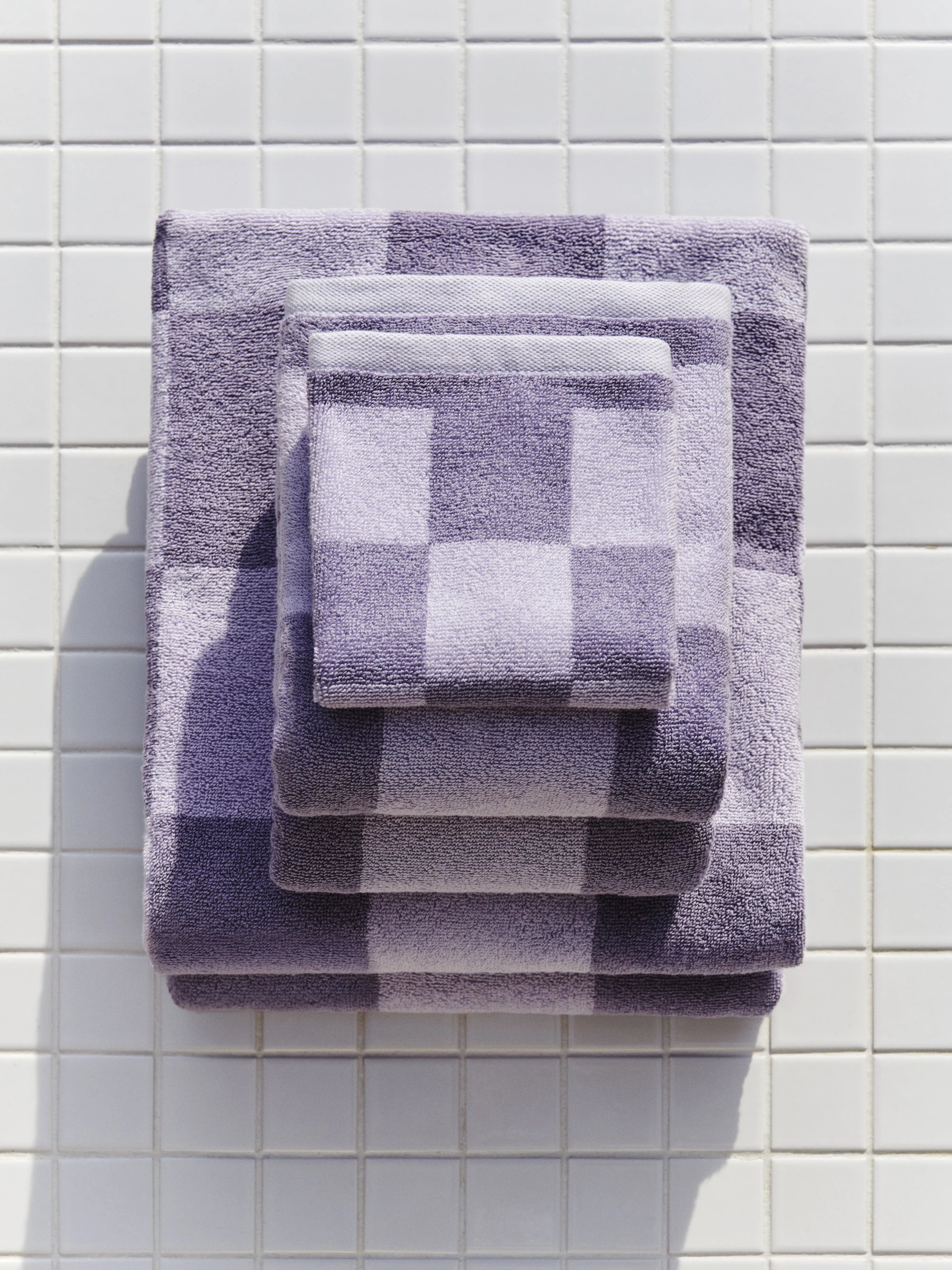 HAY Organic Cotton Check Wash Cloth and towel family in lavender stacked up on a white tiled background