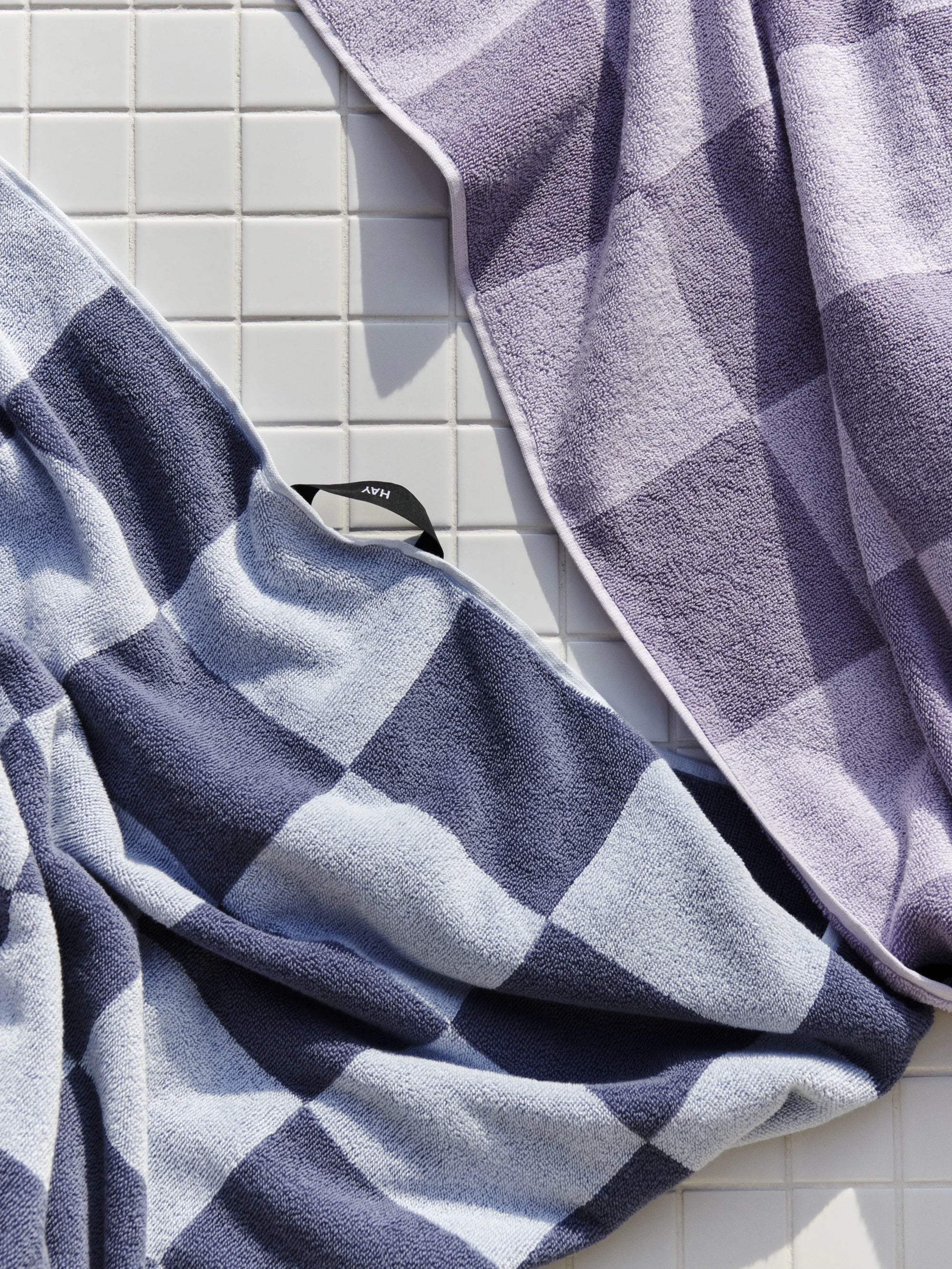 HAY Organic Cotton Check Wash Cloths in steel blue and lavender lying on a white tiled background