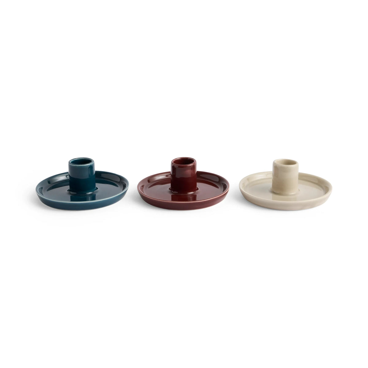 Three small ceramic HAY disc candle holders with matching round bases, shown in dark teal, chestnut brown, and warm grey on a plain white background.