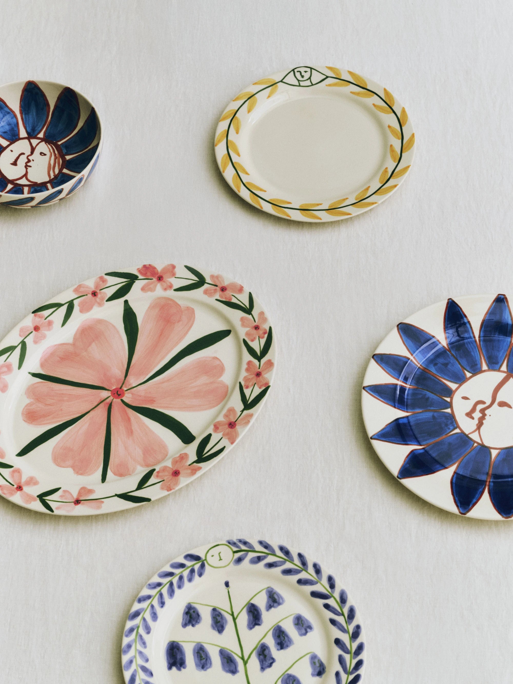 A collection of colourfully decorated plates from the HAY La Pittura collection atop a white tablecloth