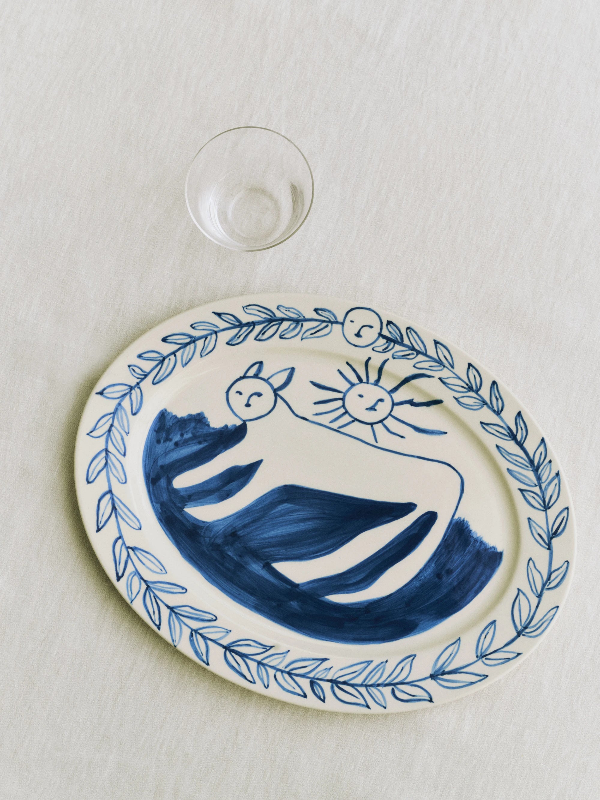 HAY x Emma Kohlmann - La Pittura Ø36.5cm Serving Platter in Charlotte on a white table cloth next to a drinking glass