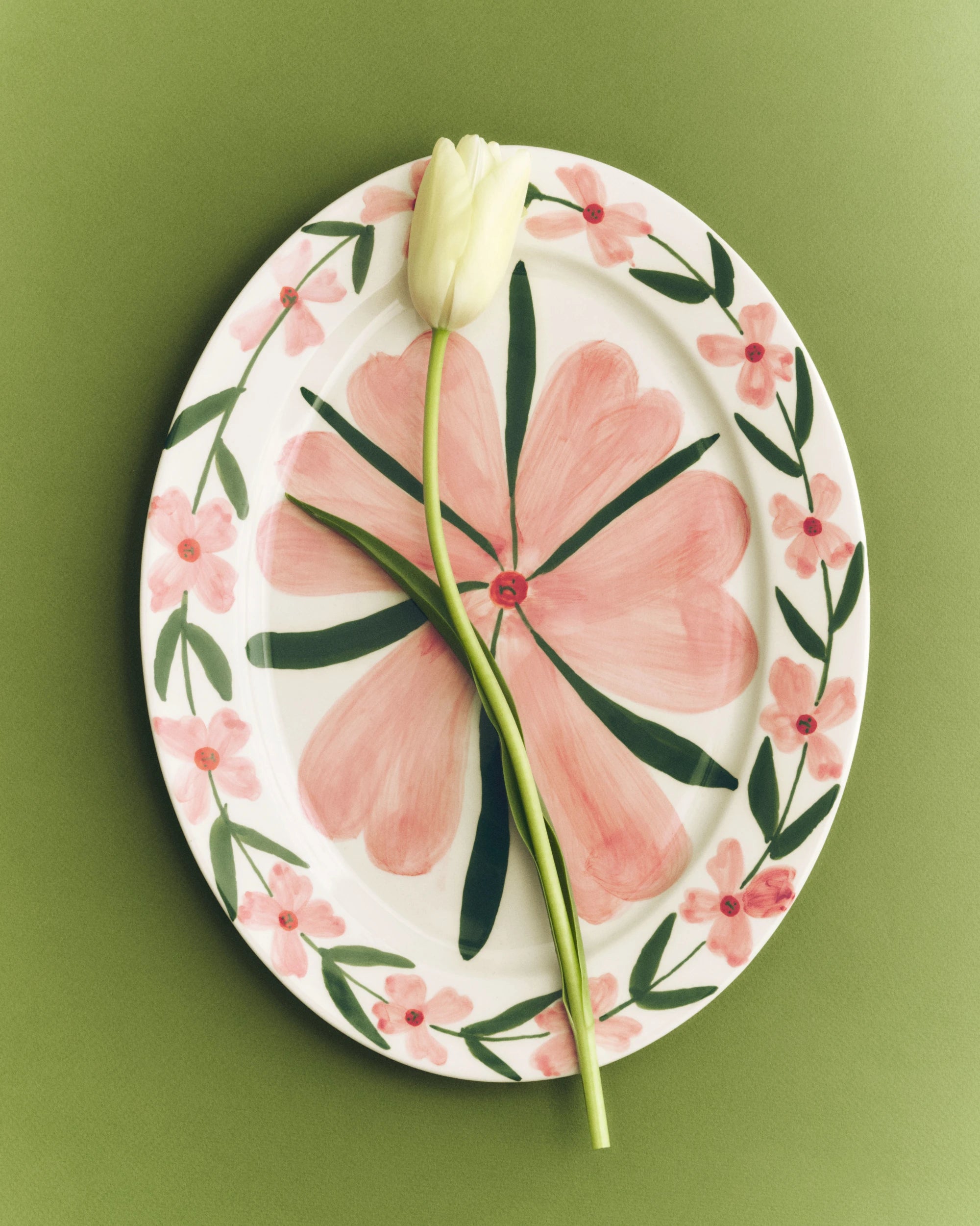 HAY x Emma Kohlmann - La Pittura Ø36.5cm Serving Platter in Josephine holding a cut white tulip against a green background