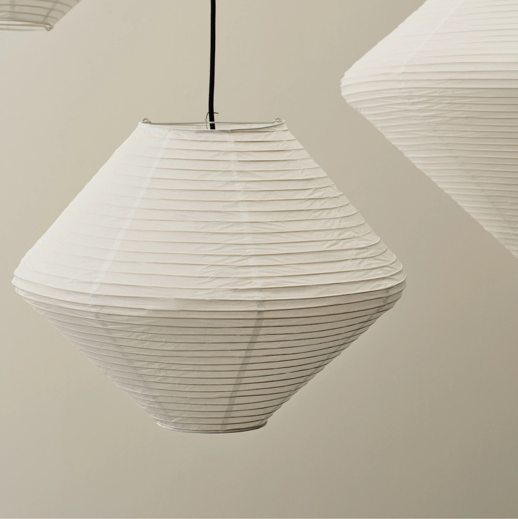 Close-up of three white paper pendant lampshades against a beige wall.