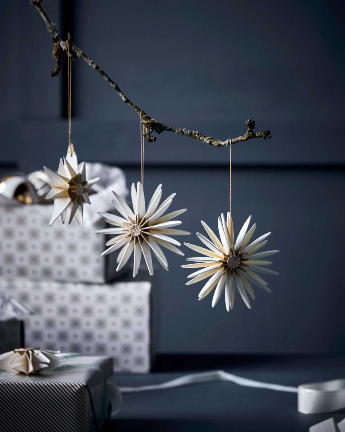 Decorative star-shaped HDStar ornaments by House Doctor, Champagne colour, hanging from a branch against a dark background.