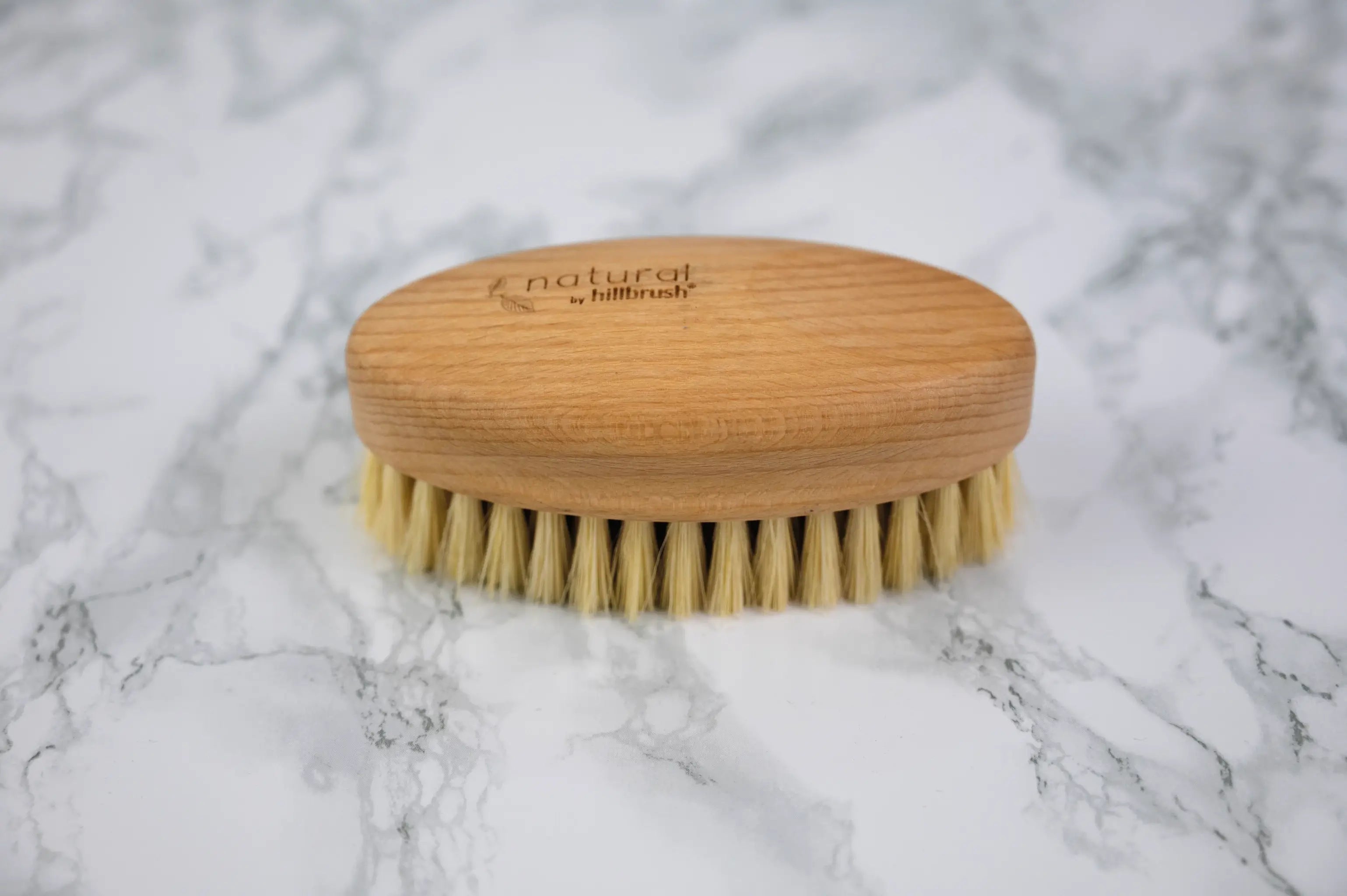 A large oval wooden vegetable brush with thick fibres sits on a marble surface. Made by UK makers Hillbrush