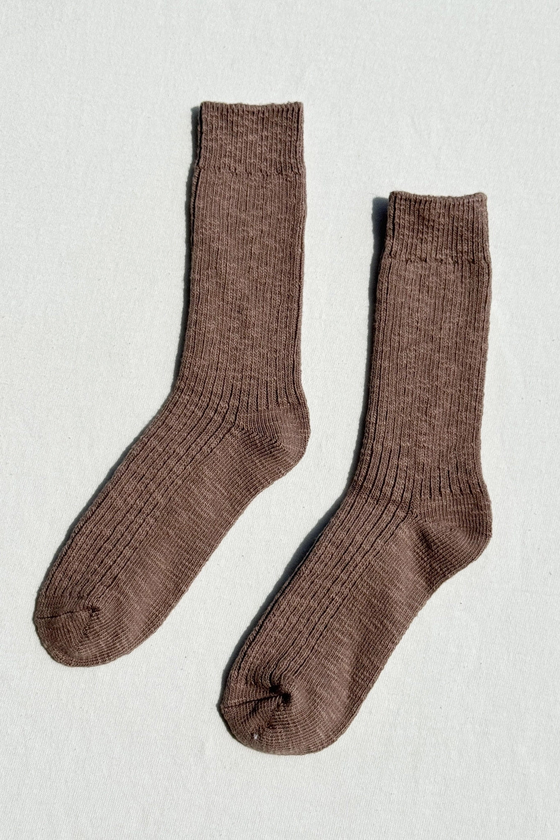 A pair of ribbed crew socks in a warm taupe-brown color, laid flat on a light textured background.