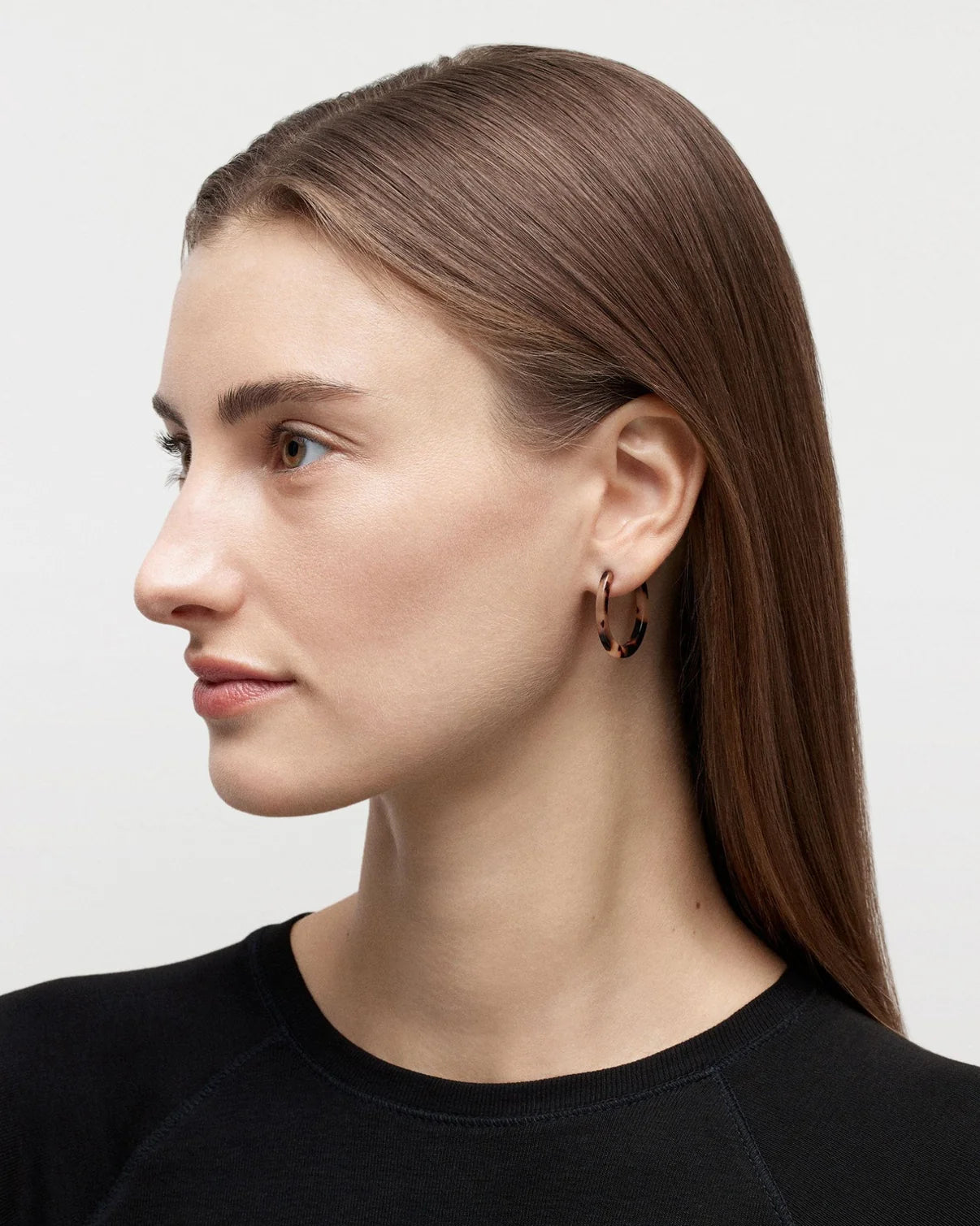 Model wearing MACHETE Mini hoops in tortoise against a bright white background