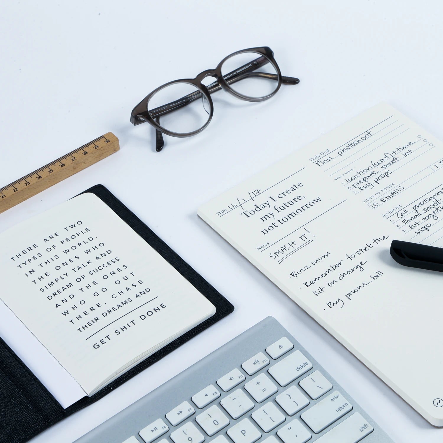 A flatlay desk scene featuring the MiGoals To Do Desk pad, a pair of glasses, keyboard and another notebook