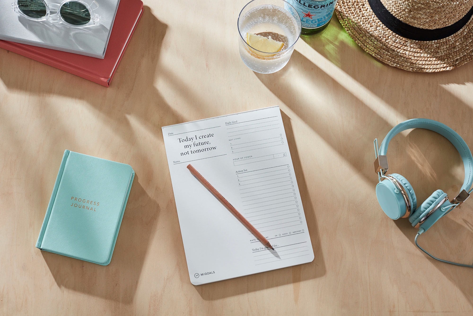 A lifestyle image of a wooden desk and personal items with the MiGoals To Do Desk pad in the centre