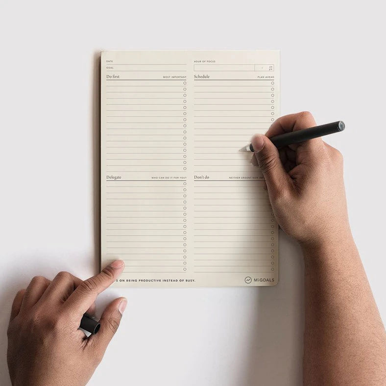A pair of mens hand holding a pen and writing on the MiGoals Focus Daily Desk Pad notebook