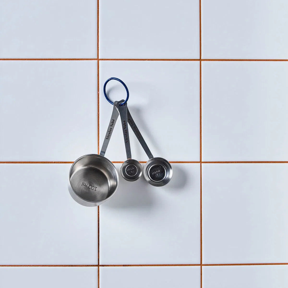 Set of metal measuring cups on a tiled wall