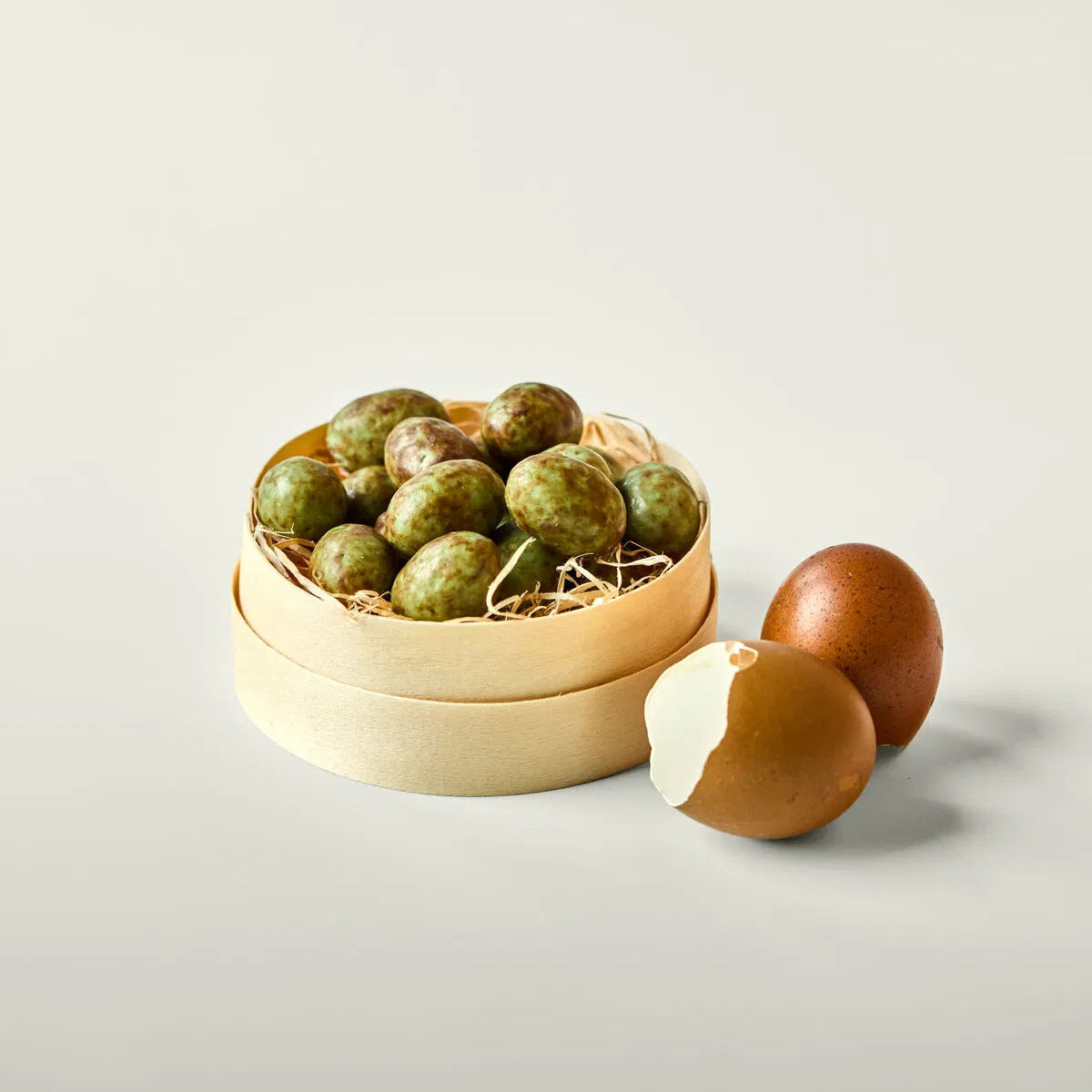 Wooden container with green and brown chocolate eggs on a light background