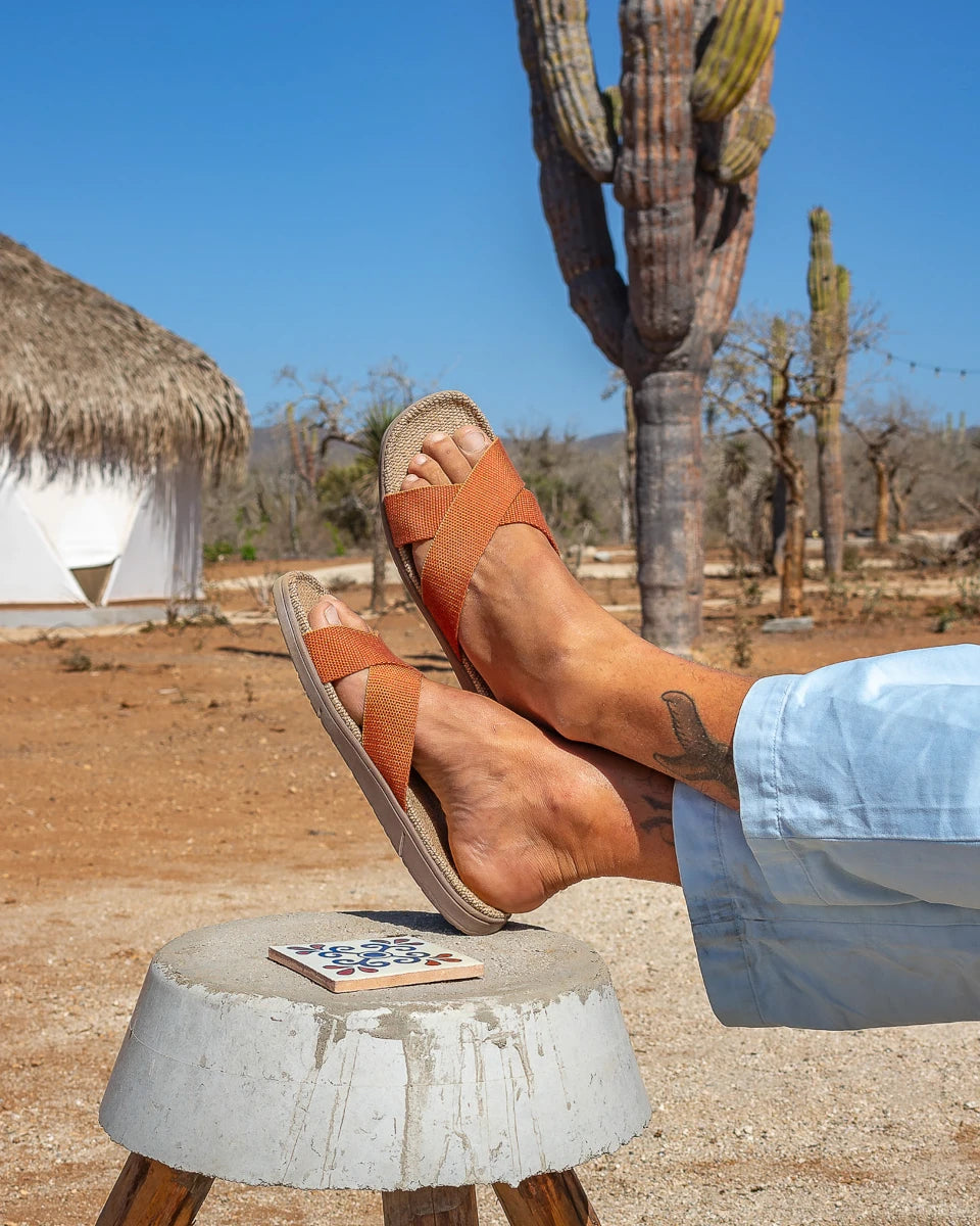 Person wearing Spicy Pumpkin Shangies sandals in a desert setting with cacti and a thatched-roof structure | Breathable Washable | Lifestory