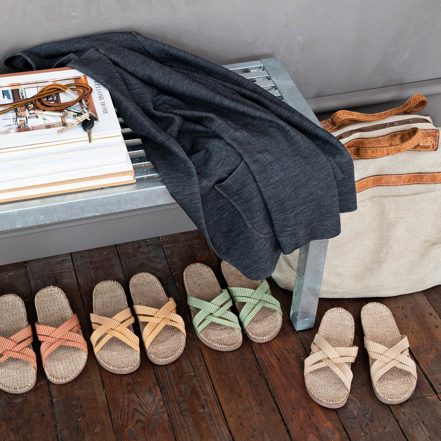 Four pairs of Shangies womens sandals in various colours. They sit on a wooden floor and under a metal bench holding books and a coat