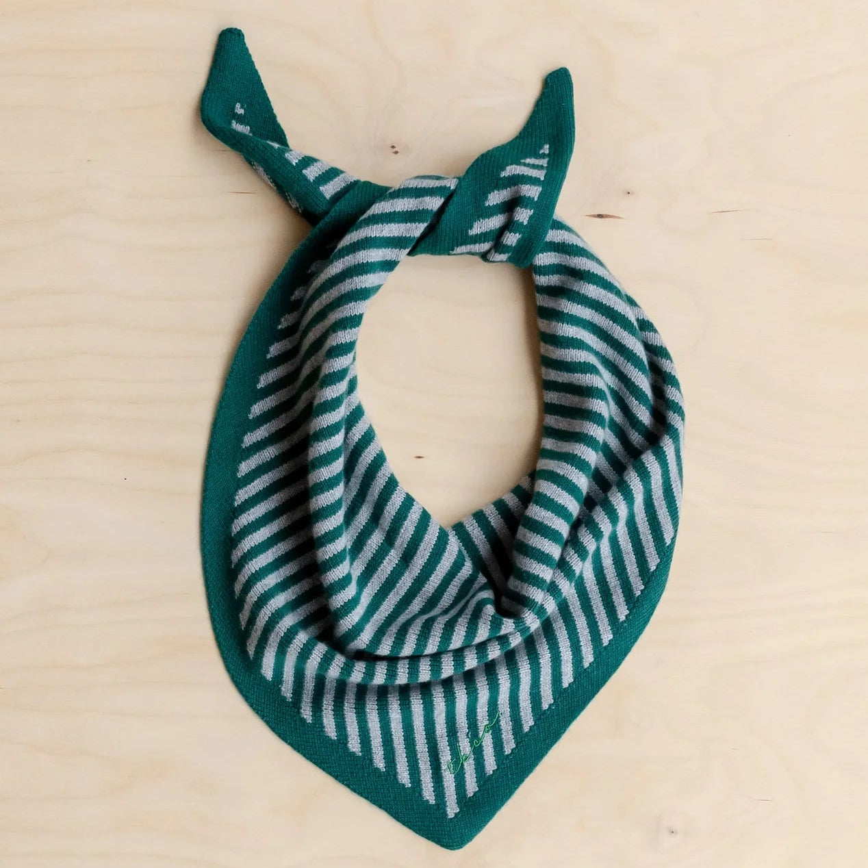 Green and grey striped merino wool scarf on a beige surface