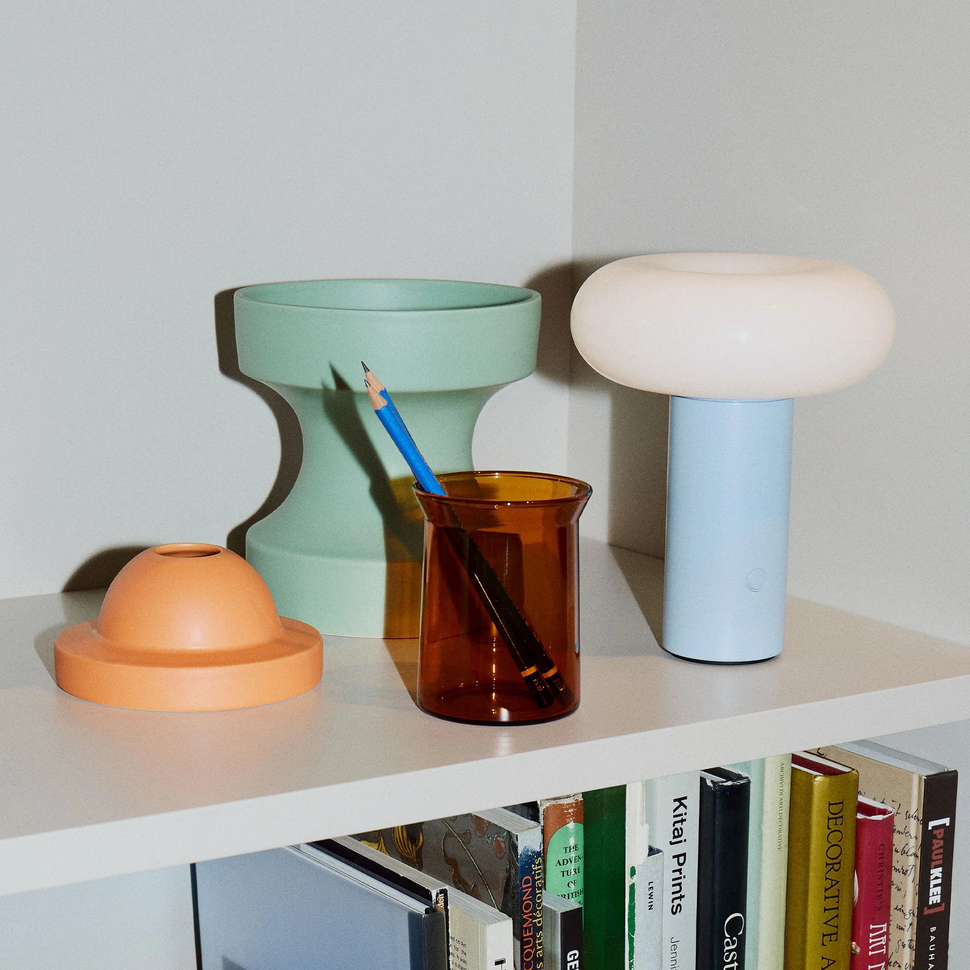 Colorful ceramic vases and a glass container on a shelf with books below.