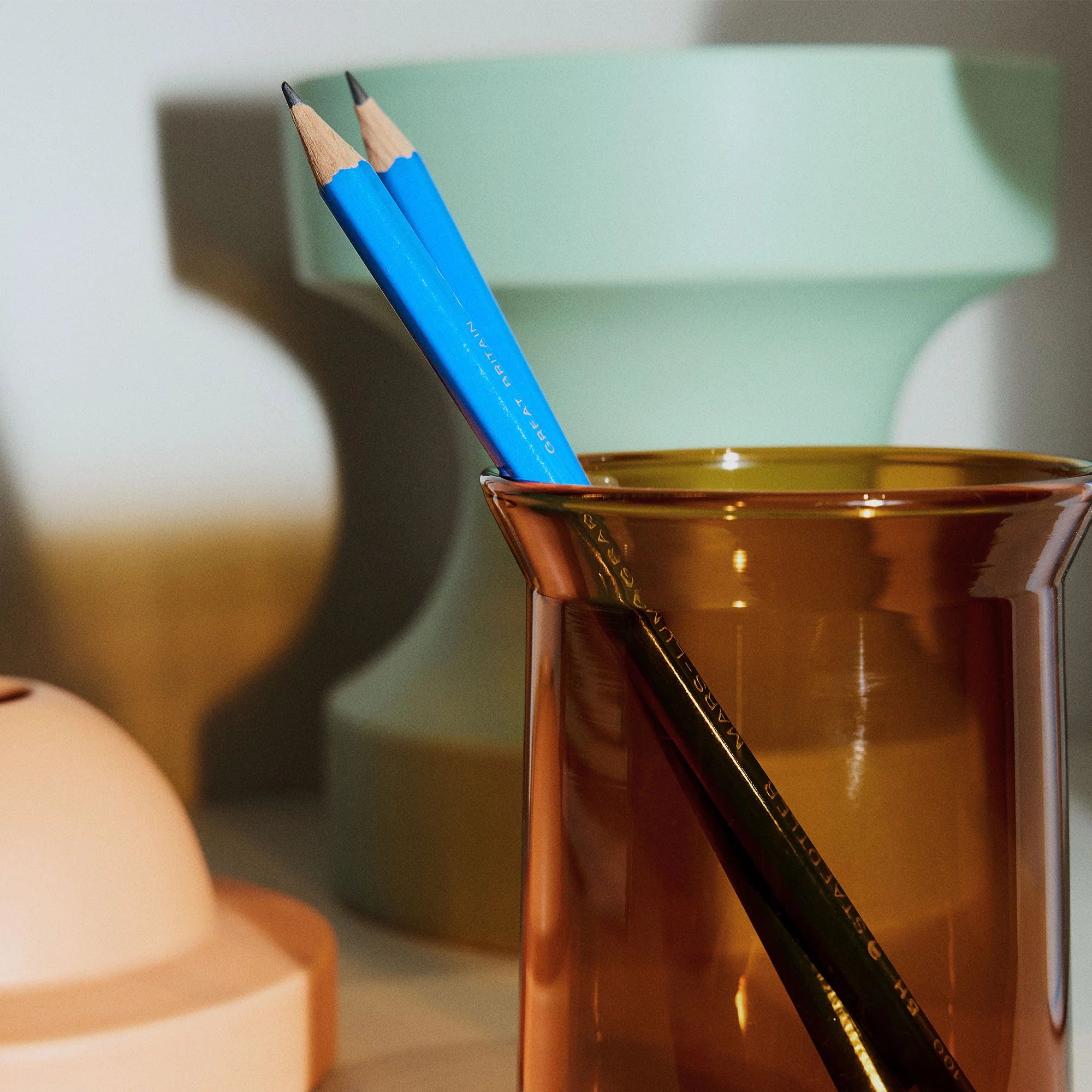 Two blue pencils in an amber glass holder with a blurred background