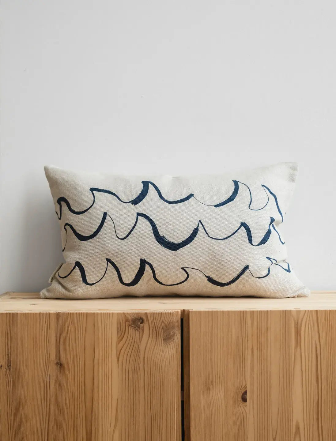 A long cushion in natural linen with a minimal blue wave shaped brush stroke motif from Fine Little Day