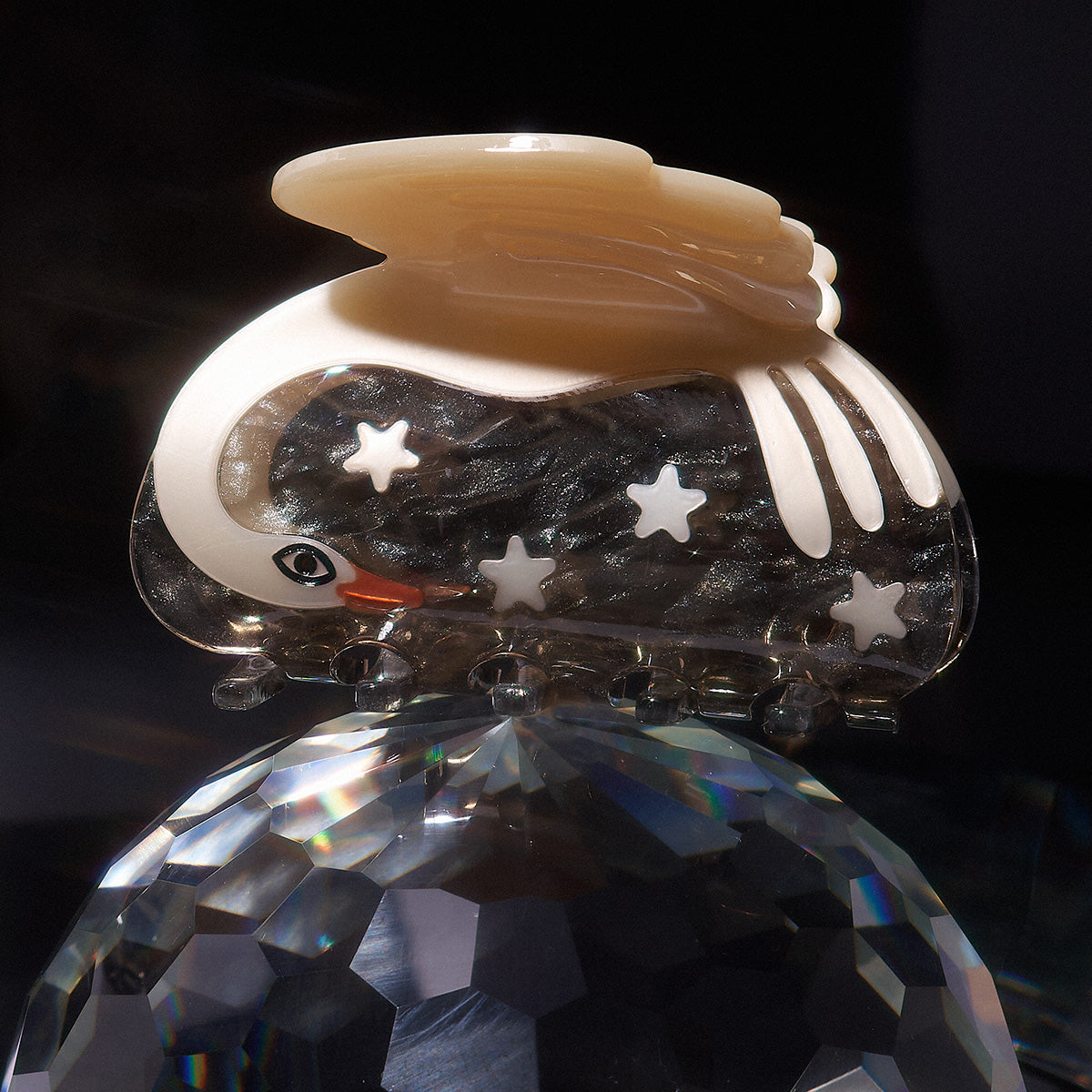 Shiny white pearl swan hair claw with star patterns on a dark background