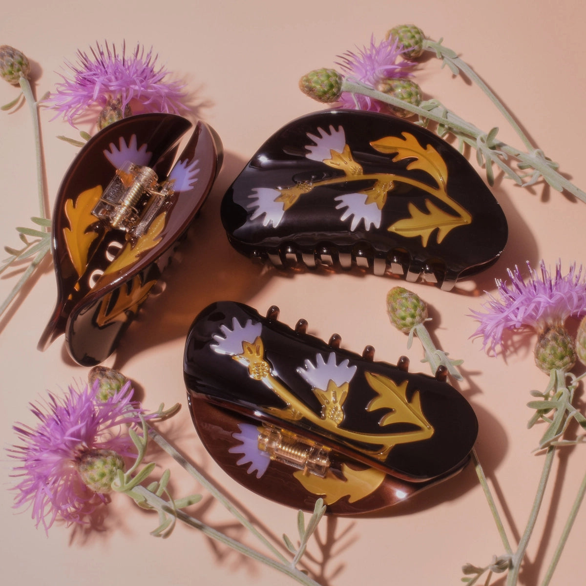 Winona Irene Milk Thistle Acetate Hair Claws on a pink surface surrounded by thistle flowers