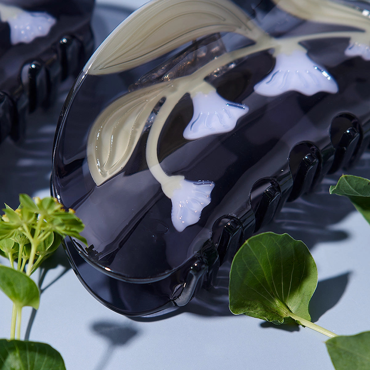 Black case with white floral design on a reflective surface with green leaves.