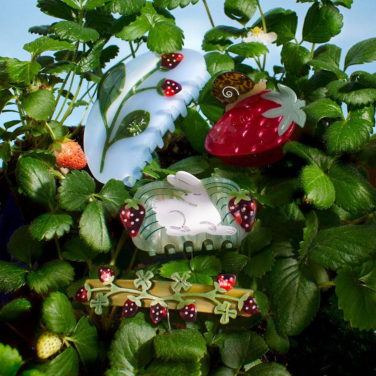 Decorative hair accessories shaped like strawberries and a rabbit among green plants.