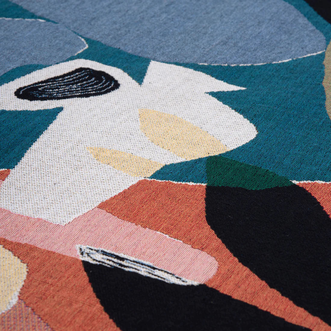 Detail shot of a colourful illustrated throw blanket in orange, greens, white and black 