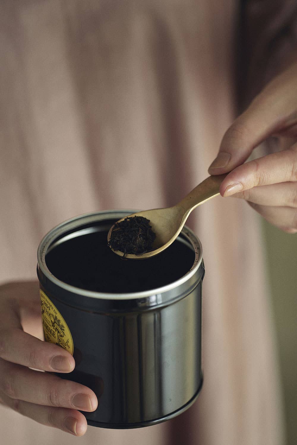 Person scooping black tea from a jar with a brass spoon