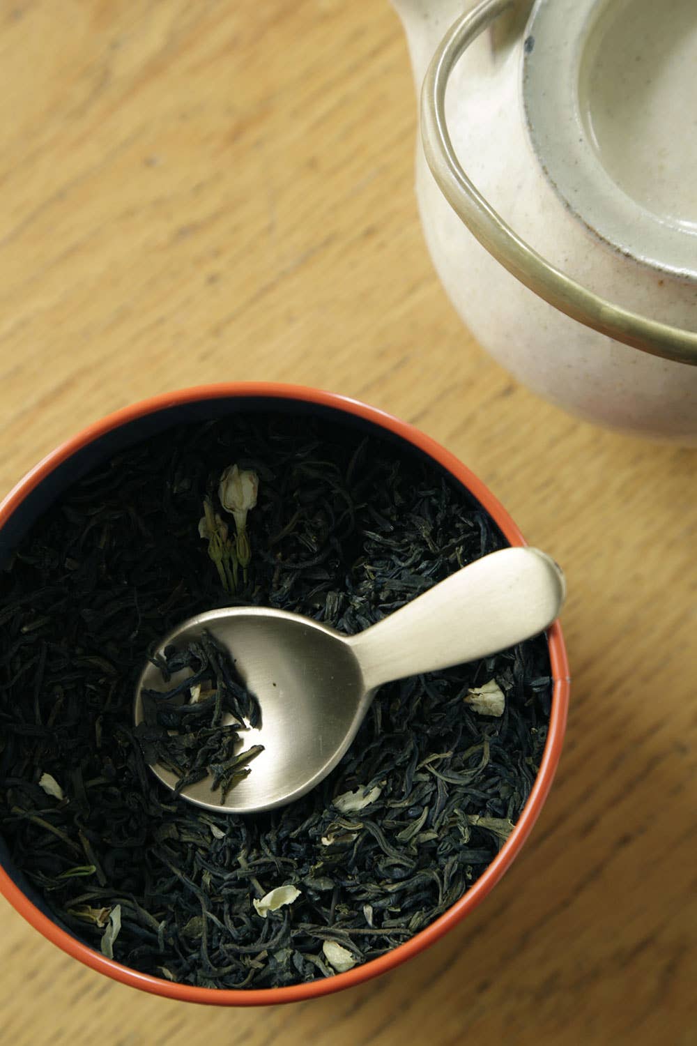 Tea leaves in a red bowl with a brass spoon on a wooden surface