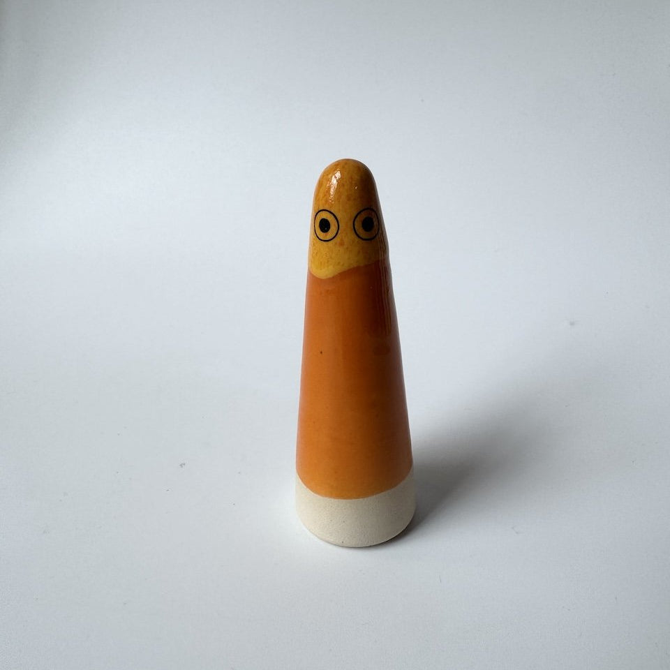 John Studio Arhoj ghost glazed orange and yellow and black-and-white eyes, and it rests on a white base.