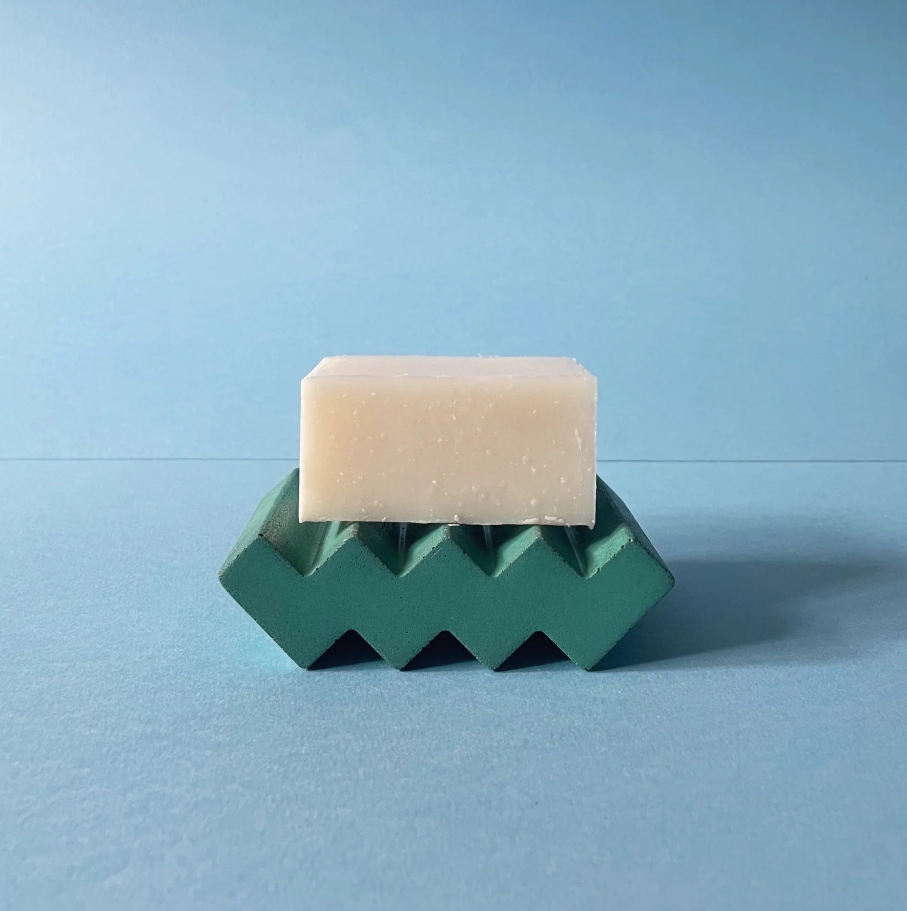Green soap dish made of cast concrete with a soap on it. Zig zag in shape, it's solid and waterproof 