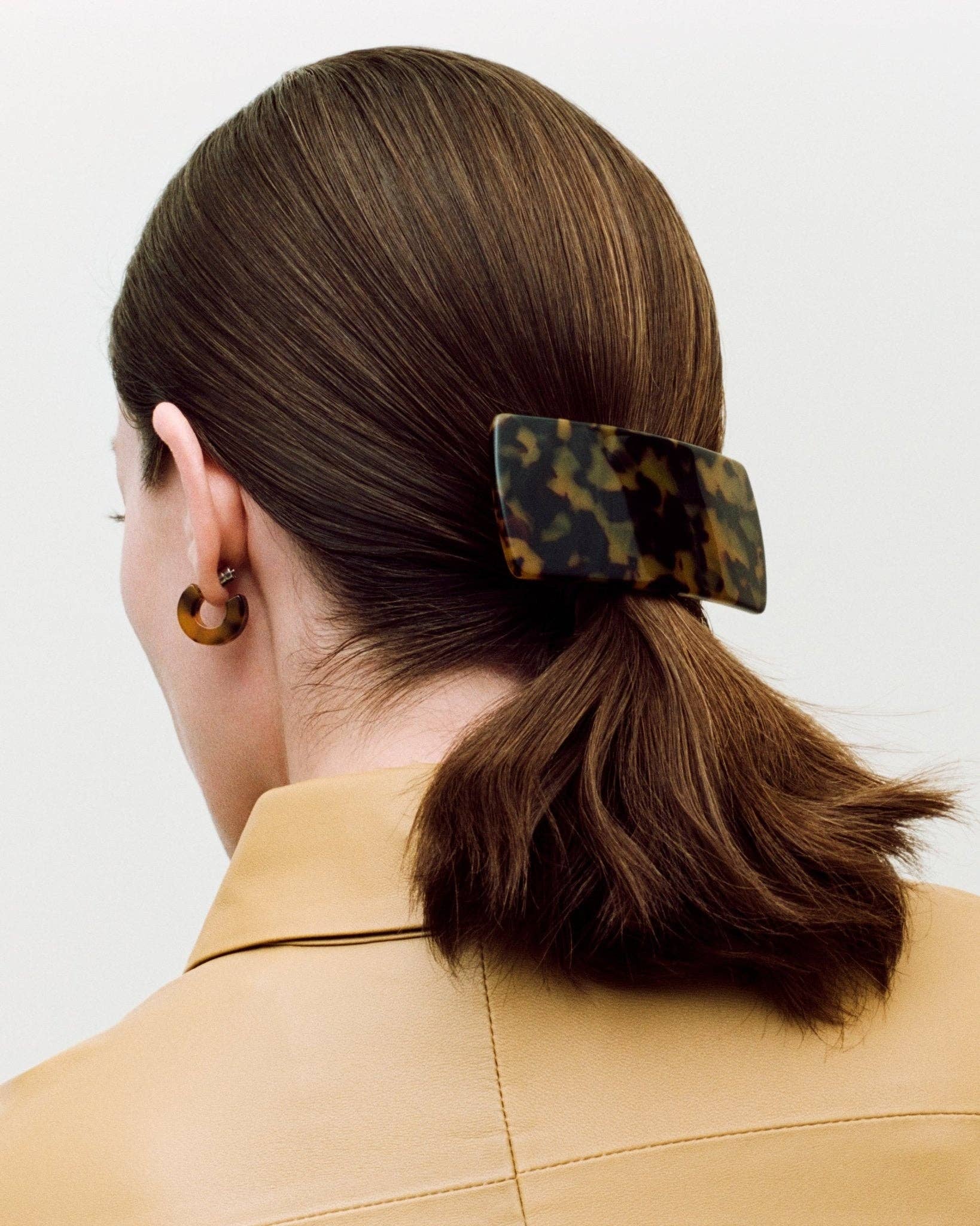 The back side head profile of a white female model with brown hair wearing the MACHETE Muse Hoops in tortoise with matching hair barrett