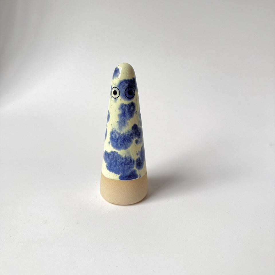 Matteo Studio Arhoj ghost featuring a cream-coloured glazed body with blue painted patterns and a natural beige wooden base, set against a plain light grey background.