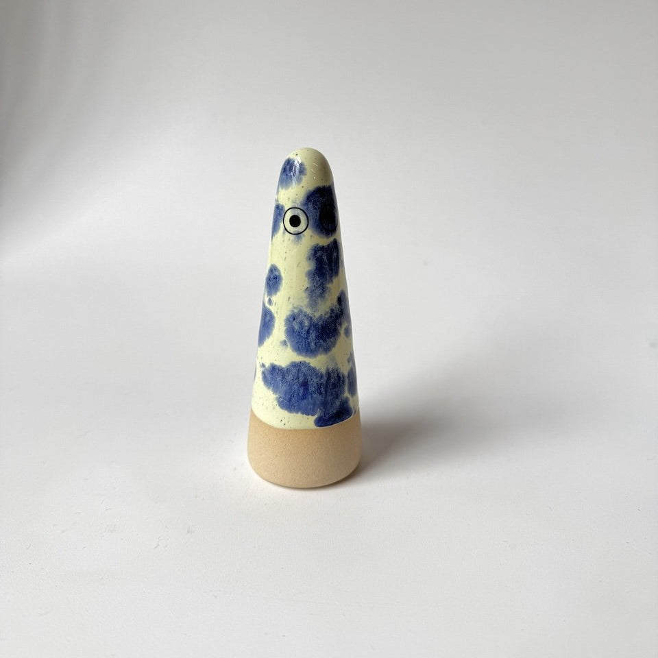 Matteo Studio Arhoj ghost featuring a cream-coloured glazed body with blue painted patterns and a natural beige wooden base, set against a plain light grey background.