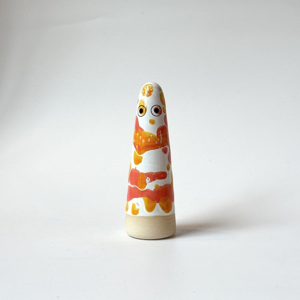 Princess Studio Arhoj ghost in orange, yellow, and white on a beige base, standing on a white surface against a light grey background.