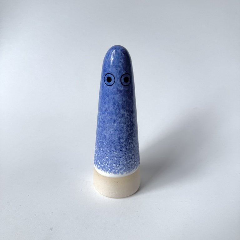 Aqualife Studio Arhoj ghost with blue speckled glaze with a beige base and simple black eyes, photographed on a plain light grey background.