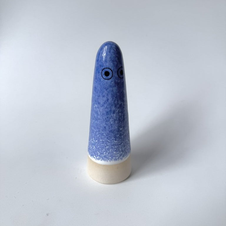 Aqualife Studio Arhoj ghost with blue speckled glaze with a beige base and simple black eyes, photographed on a plain light grey background.