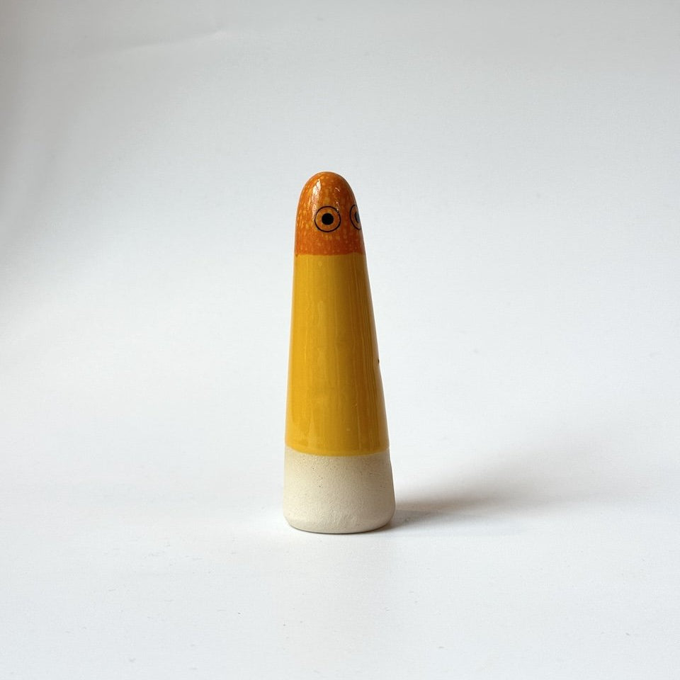 Layla Studio Arhoj ghost in orange and yellow glaze on a beige base, standing on a white surface against a light grey background.